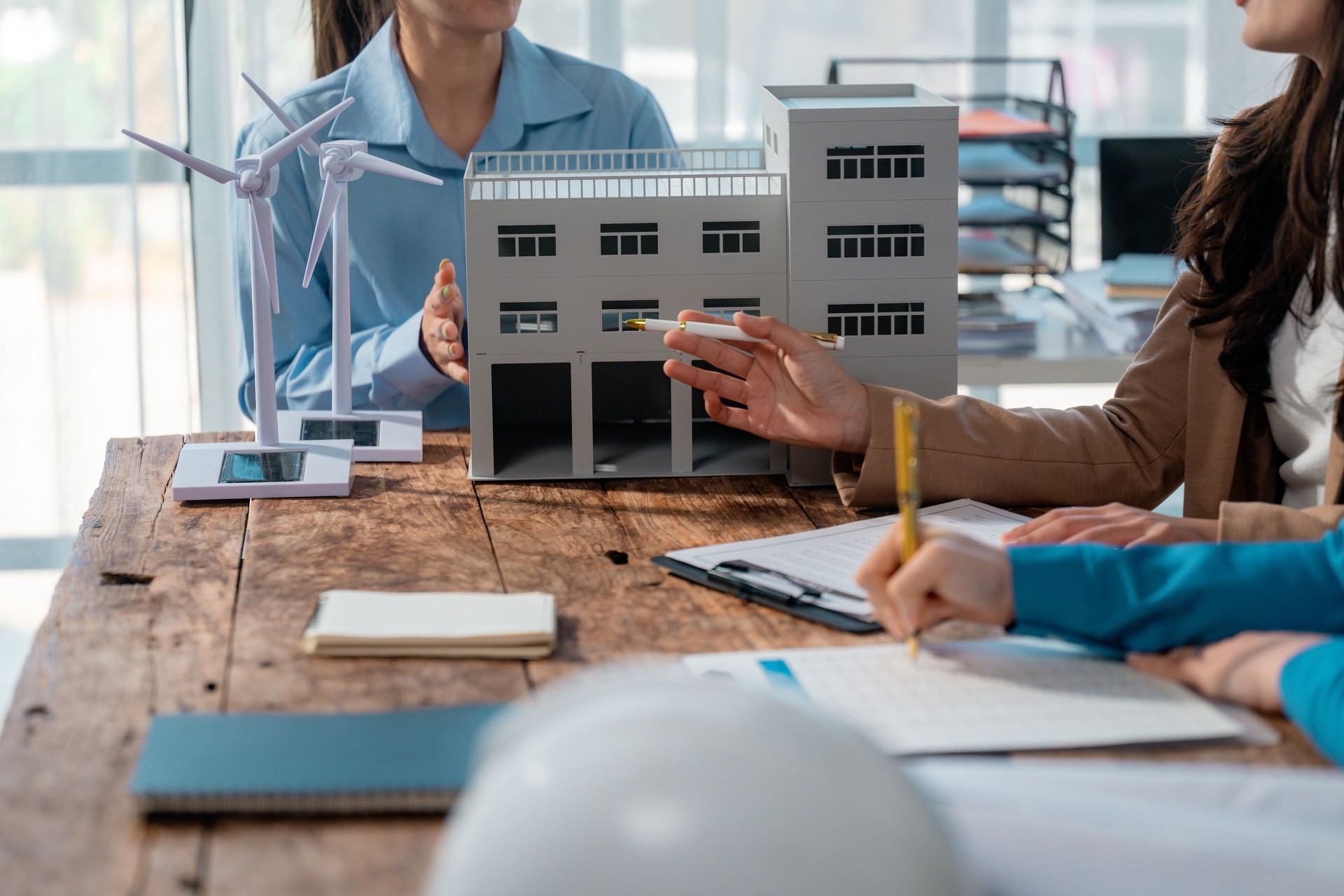 Professional engineers collaborating in conference room, analyzing sustainable building design, integrating renewable wind and solar energy technologies