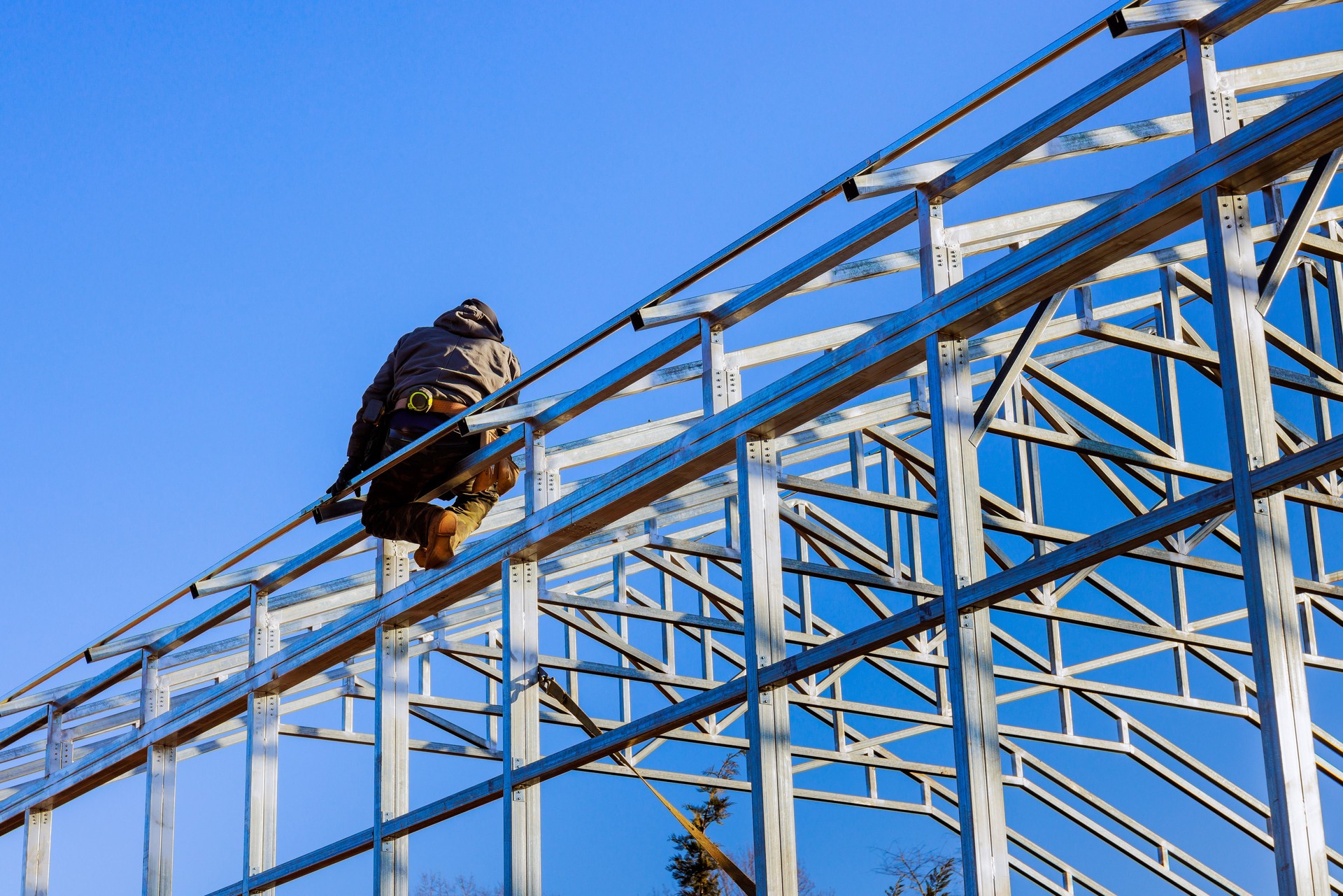 Construction worker builds metal frame of greenhouse under clear blue sky during daytime