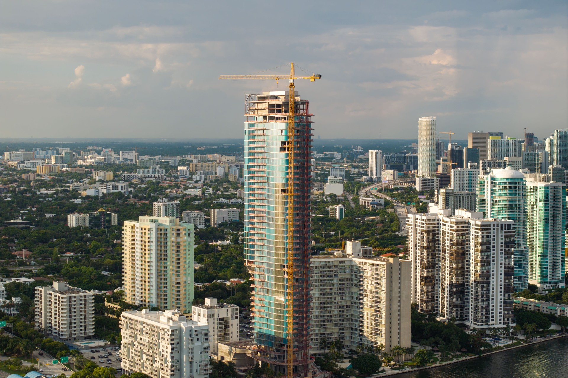 Real estate development in Miami urban area. Tower lifting crane at high residential apartment building construction site