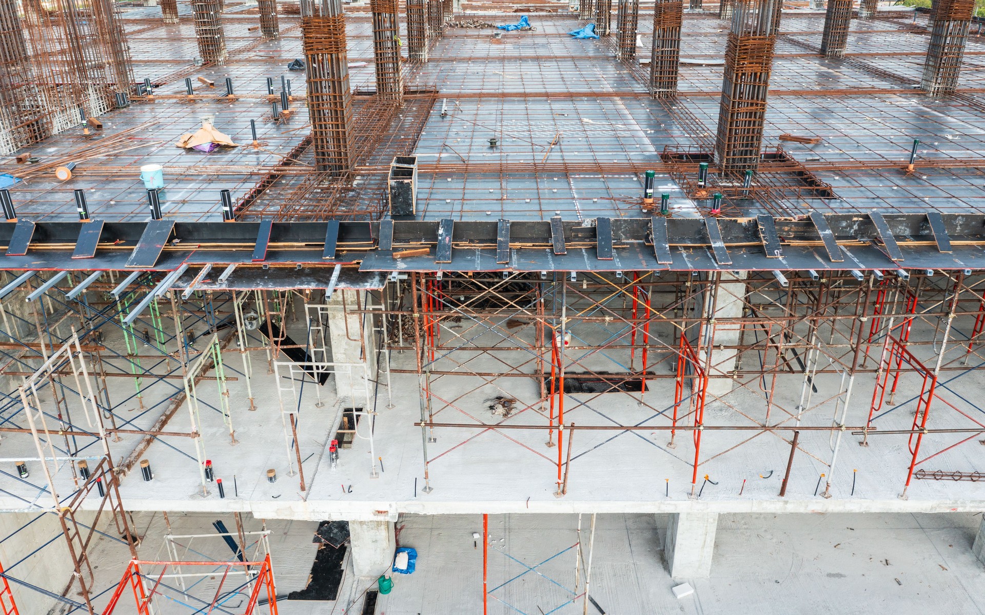 aerial view of a multi-level construction site, showcasing steel rebar on the upper floor, reinforced concrete columns, the progression of a building under construction.
